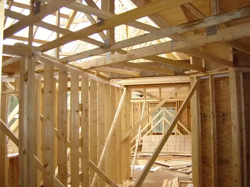 Interior of a house under construction with yellow pine studs, diagonal bracing, and engineered roof trusses.