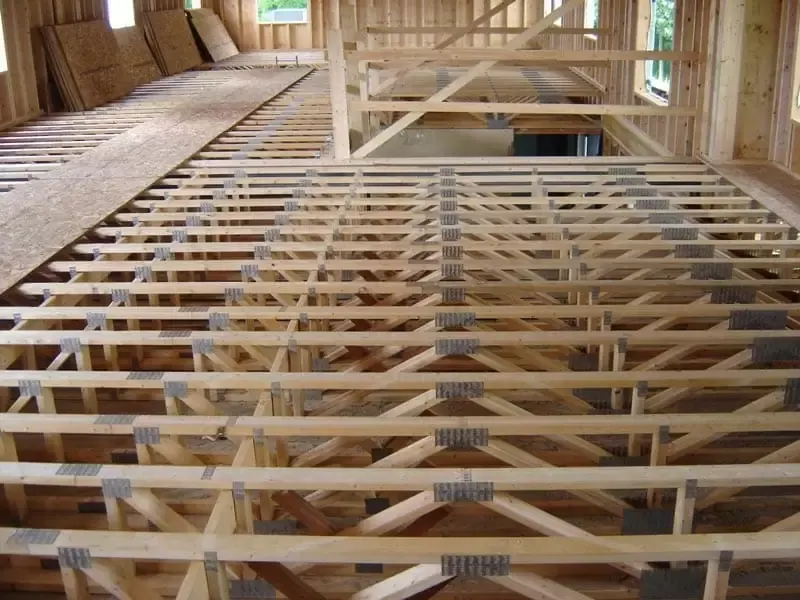 Overhead view of engineered wood floor trusses with metal connector plates and OSB subfloor sheets.