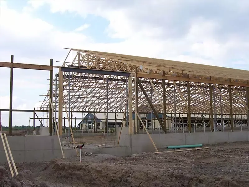 Exterior wide-angle view of a massive wooden roof truss system for a new barn under construction.
