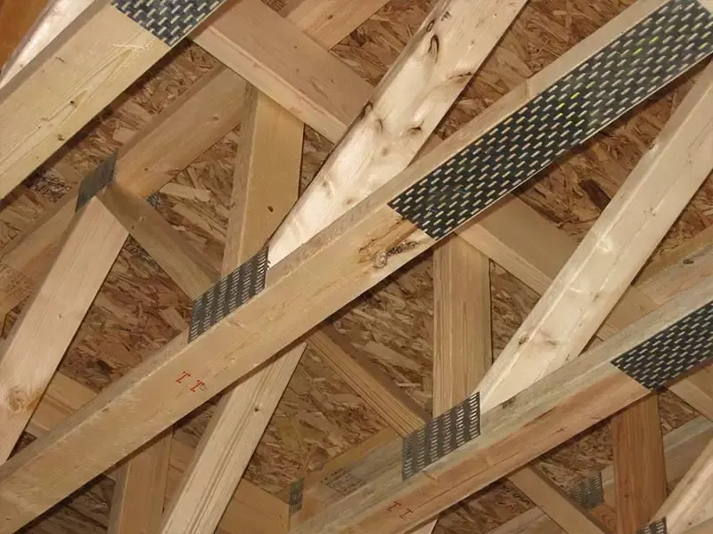 Close-up of metal gusset plates connecting wooden roof trusses with OSB sheathing in the background.
