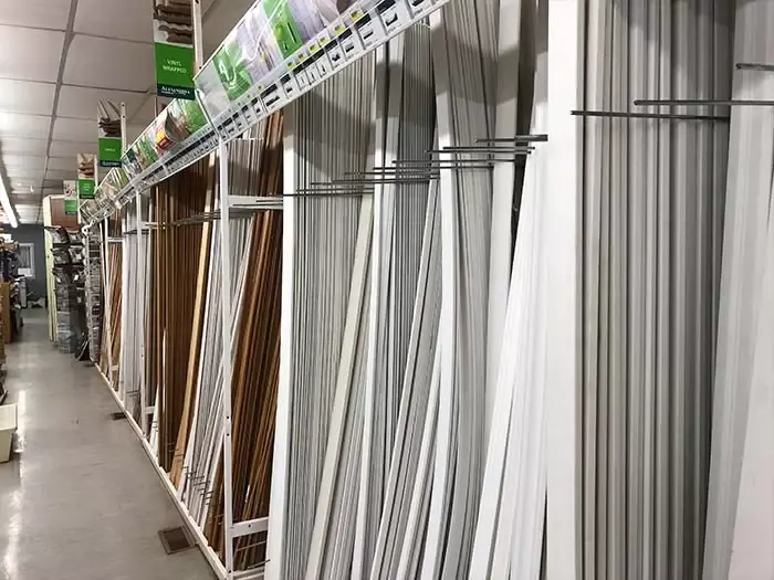 A retail aisle at Great Lakes Rona featuring vertical racks of white baseboard, crown moulding, and wooden trim profiles.