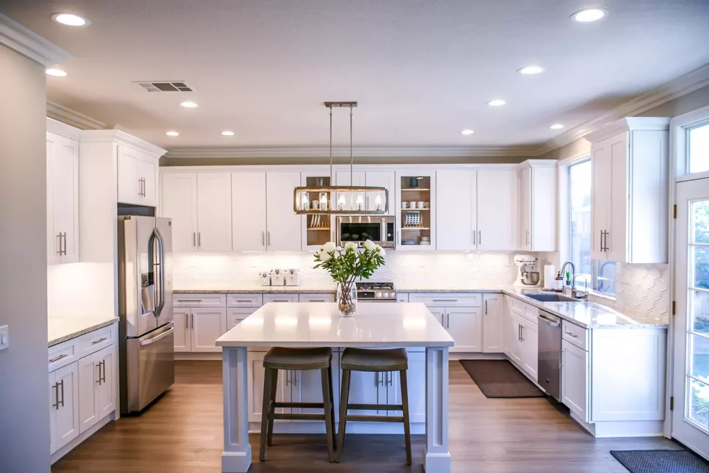 A bright, spacious kitchen featuring white shaker cabinets, a large central island with seating, stainless steel appliances, and recessed lighting.