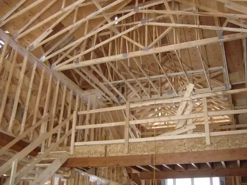 Interior wood framing of a multi-level house showing complex roof trusses, wall studs, and a temporary wooden staircase.