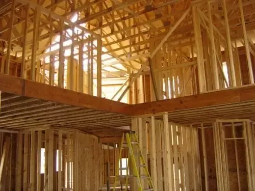 Interior view of a two-story house frame showing wall studs, floor joists, and roof trusses.