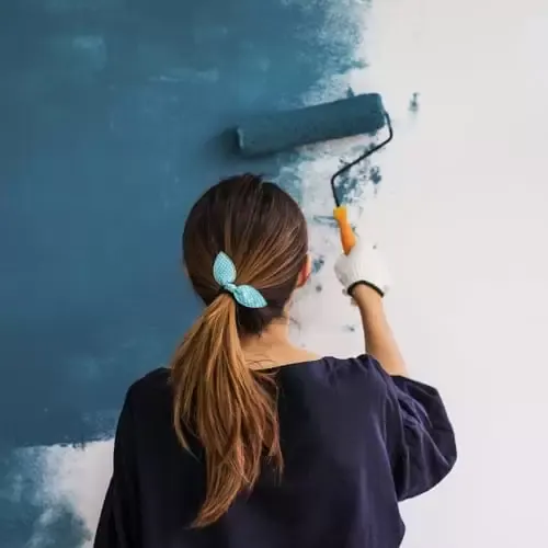 Woman painting wall blue with a paint roller.